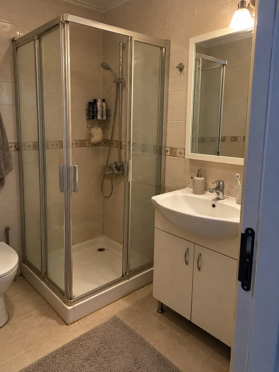 Tadilat öncesi bej fayanslı eski duşakabin ve lavabo dolaplı banyo