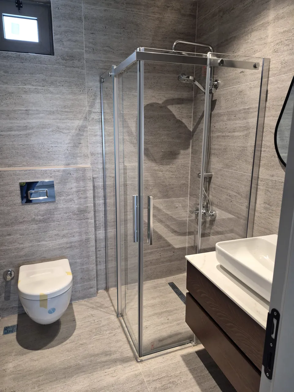 Traverten görünümlü gri seramik, duşakabin ve asma dolaplı tamamlanmış banyo